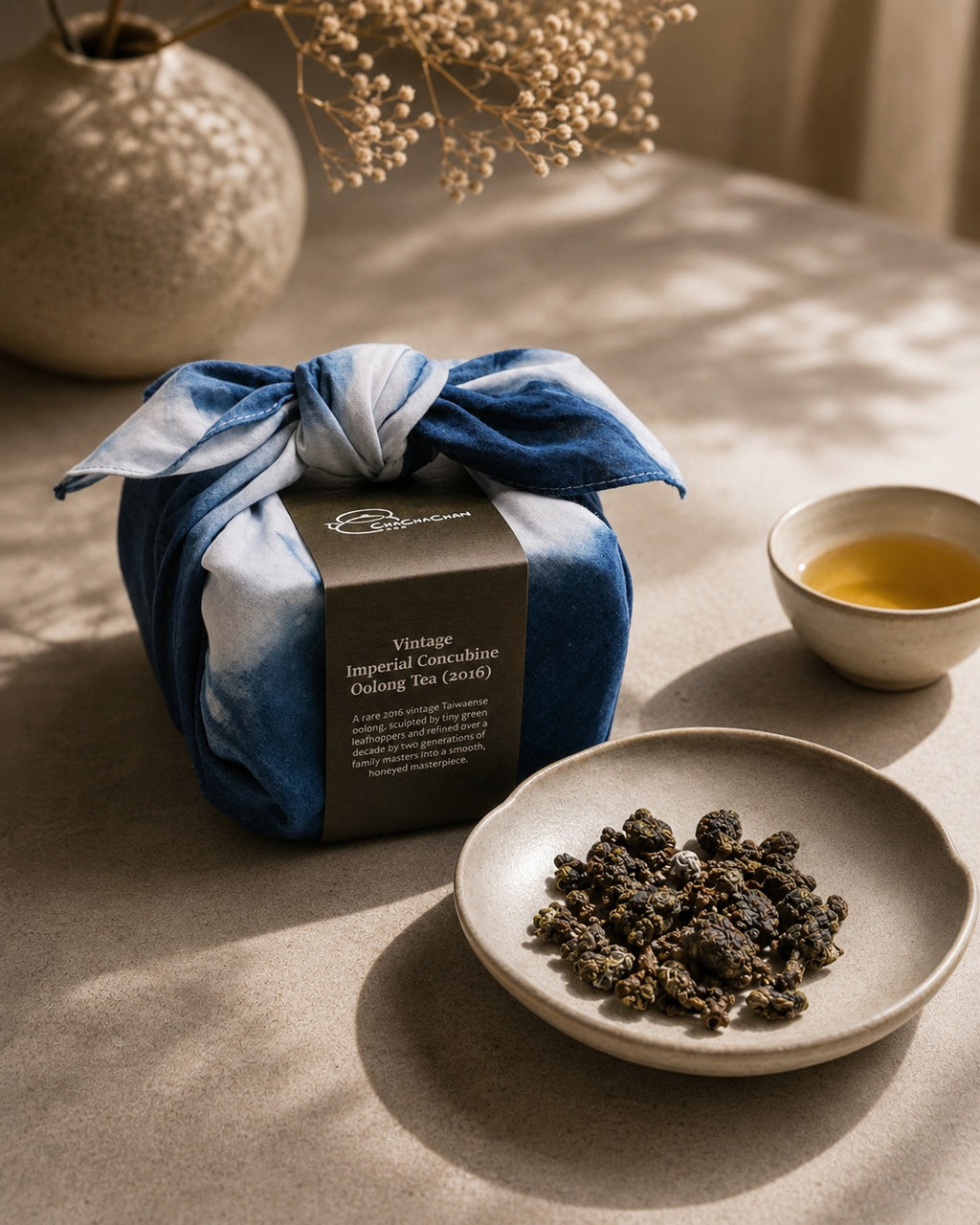A wrapped tea gift box tied with a blue and white tie-dye furokshiki cloth, featuring a dark brown paper band labelled 'Vintage Imperial Concubine Oolong Tea (2016)' from Cha Cha Chan.