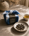 A wrapped tea gift box tied with a blue and white tie-dye furokshiki cloth, featuring a dark brown paper band labelled 'Vintage Imperial Concubine Oolong Tea (2016)' from Cha Cha Chan.
