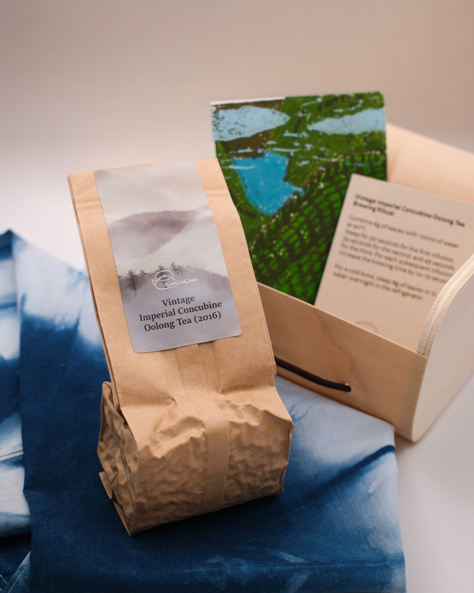 A wrapped tea gift box tied with a blue and white tie-dye furokshiki cloth, featuring a linocut postcard in the design of tea fields. This is the 'Vintage Imperial Concubine Oolong Tea (2016)' from Cha Cha Chan.