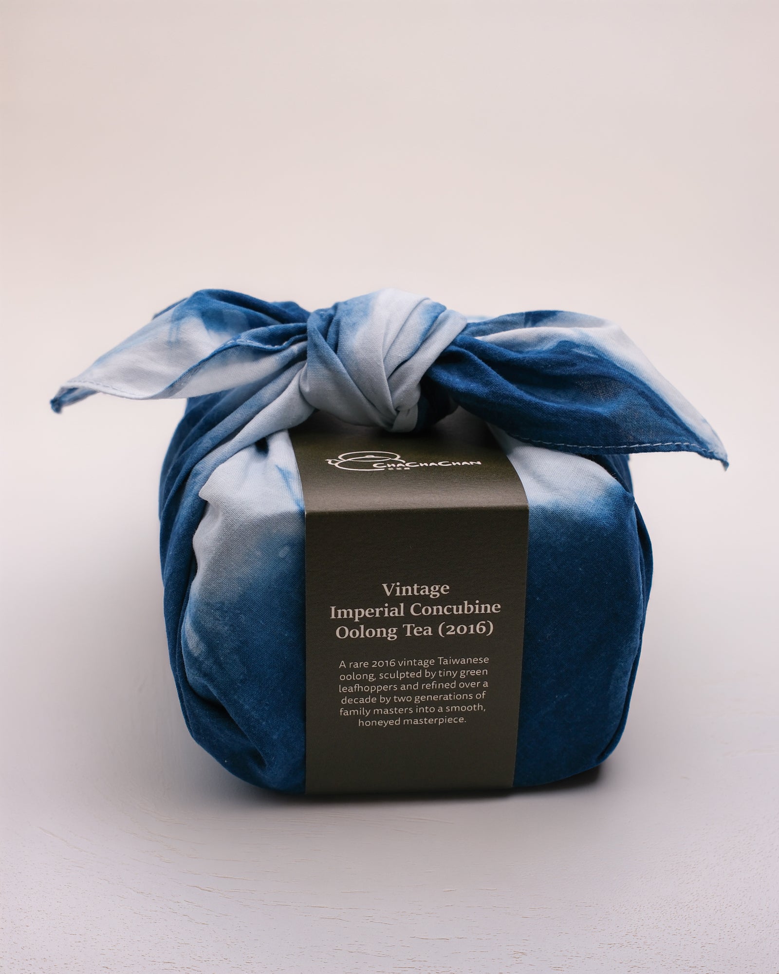 A wrapped tea gift box tied with a blue and white tie-dye furokshiki cloth, featuring a dark brown paper band labelled 'Vintage Imperial Concubine Oolong Tea (2016)' from Cha Cha Chan.