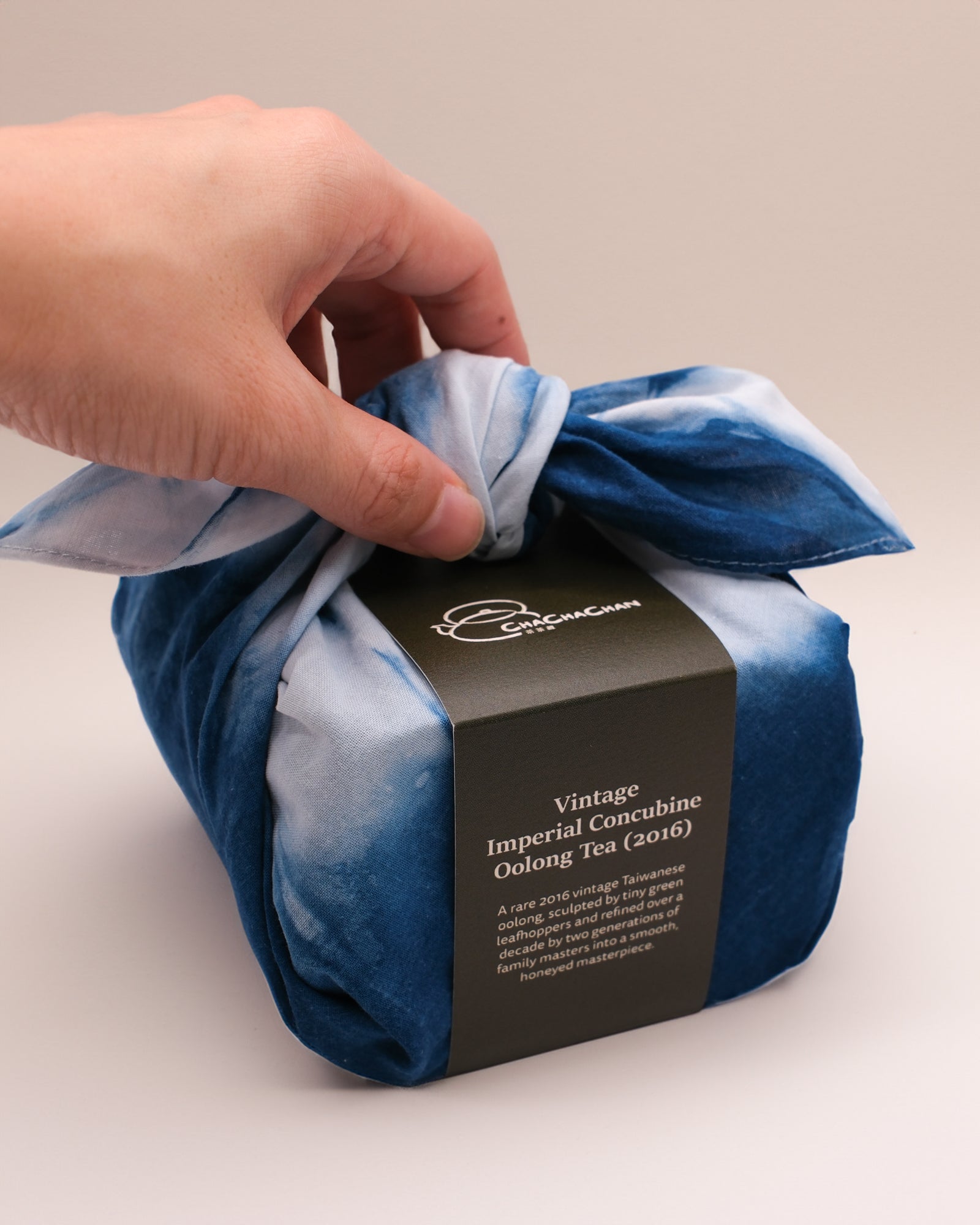 A wrapped tea gift box tied with a blue and white tie-dye furokshiki cloth, featuring a dark brown paper band labelled 'Vintage Imperial Concubine Oolong Tea (2016)' from Cha Cha Chan.