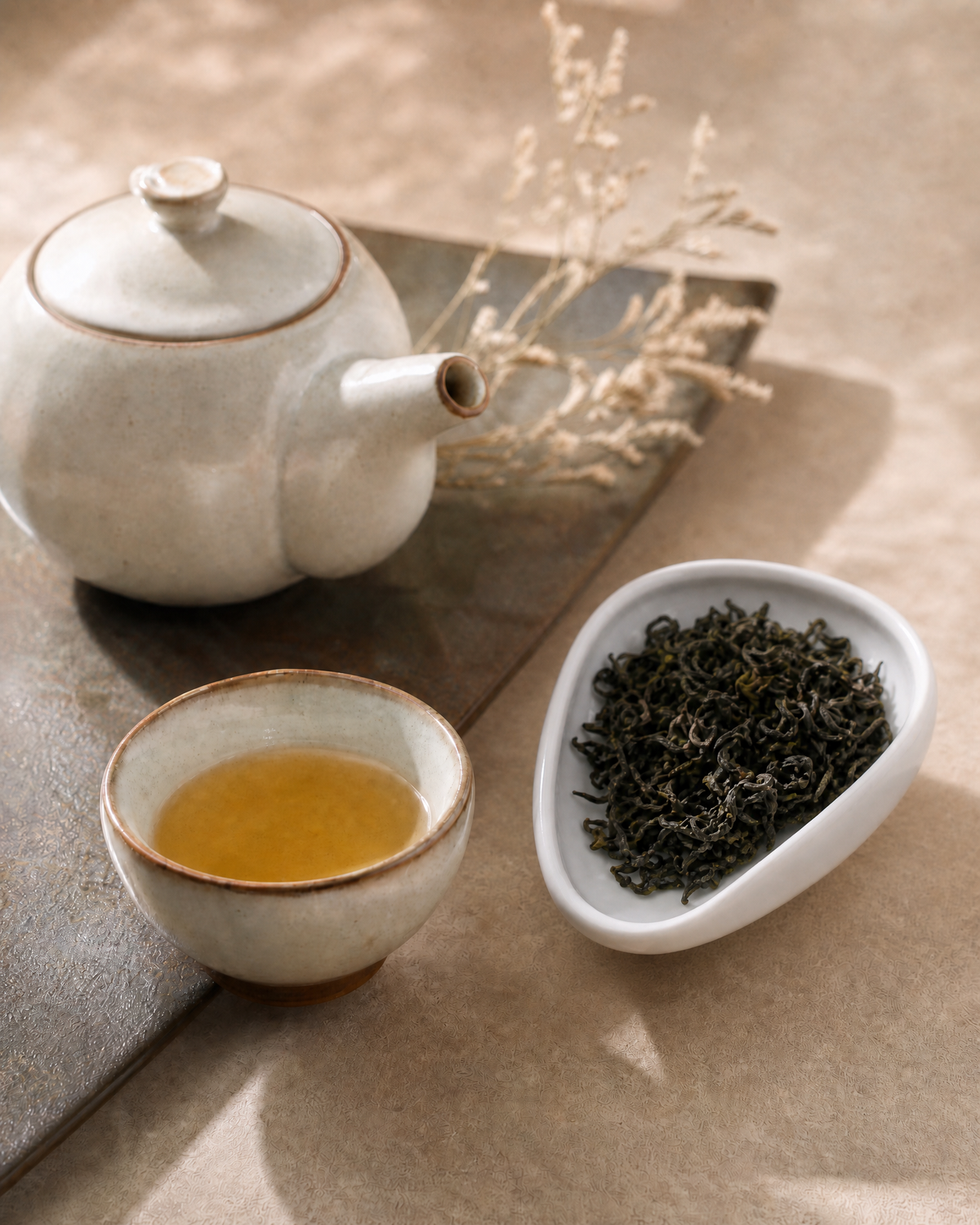 A ceramic teapot and matching cup filled with Mengding Yellow Tea, arranged on a tray beside a small dish of loose-leaf tea on a neutral beige surface.