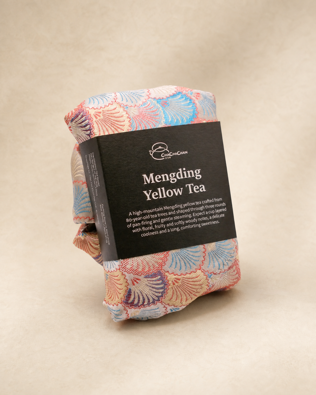 A packaged folded tea bag with a black label reading 'Mengding Yellow Tea' and a pastel seashell pattern from Cha Cha Chan on a beige background.