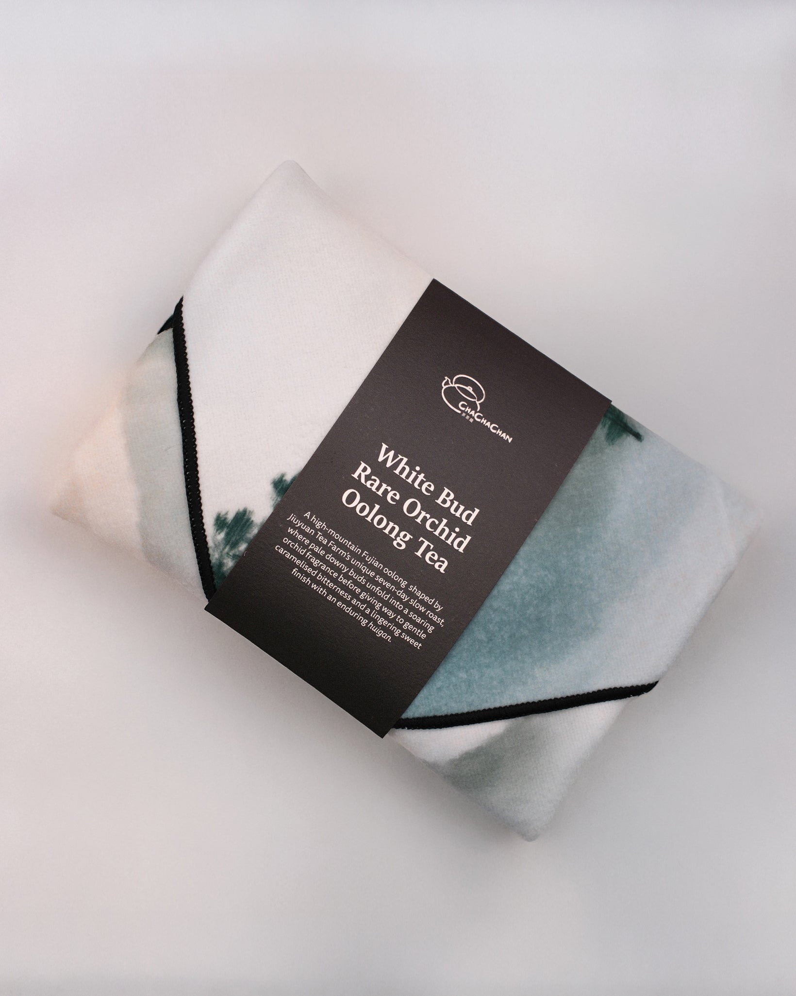 Gift tea set for the 'White Bud Orchid Oolong Tea' from Cha Cha Chan, featuring a packet of loose tea leaves, a postcard, and a reusable magic wrap.