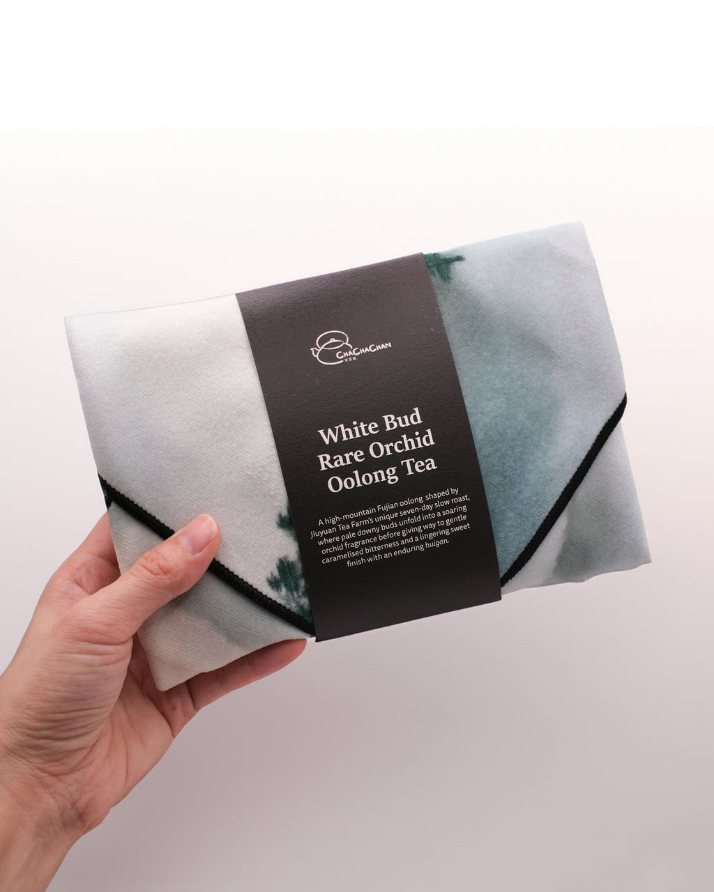 Gift tea set for the 'White Bud Orchid Oolong Tea' from Cha Cha Chan, featuring a packet of loose tea leaves, a postcard, and a reusable magic wrap.