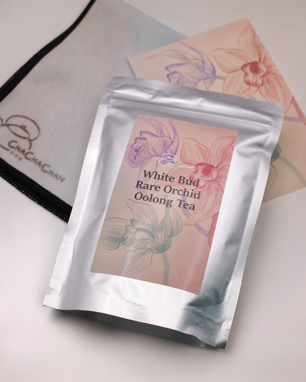 Gift tea set for the 'White Bud Orchid Oolong Tea' from Cha Cha Chan, featuring a packet of loose tea leaves, a postcard, and a reusable magic wrap.