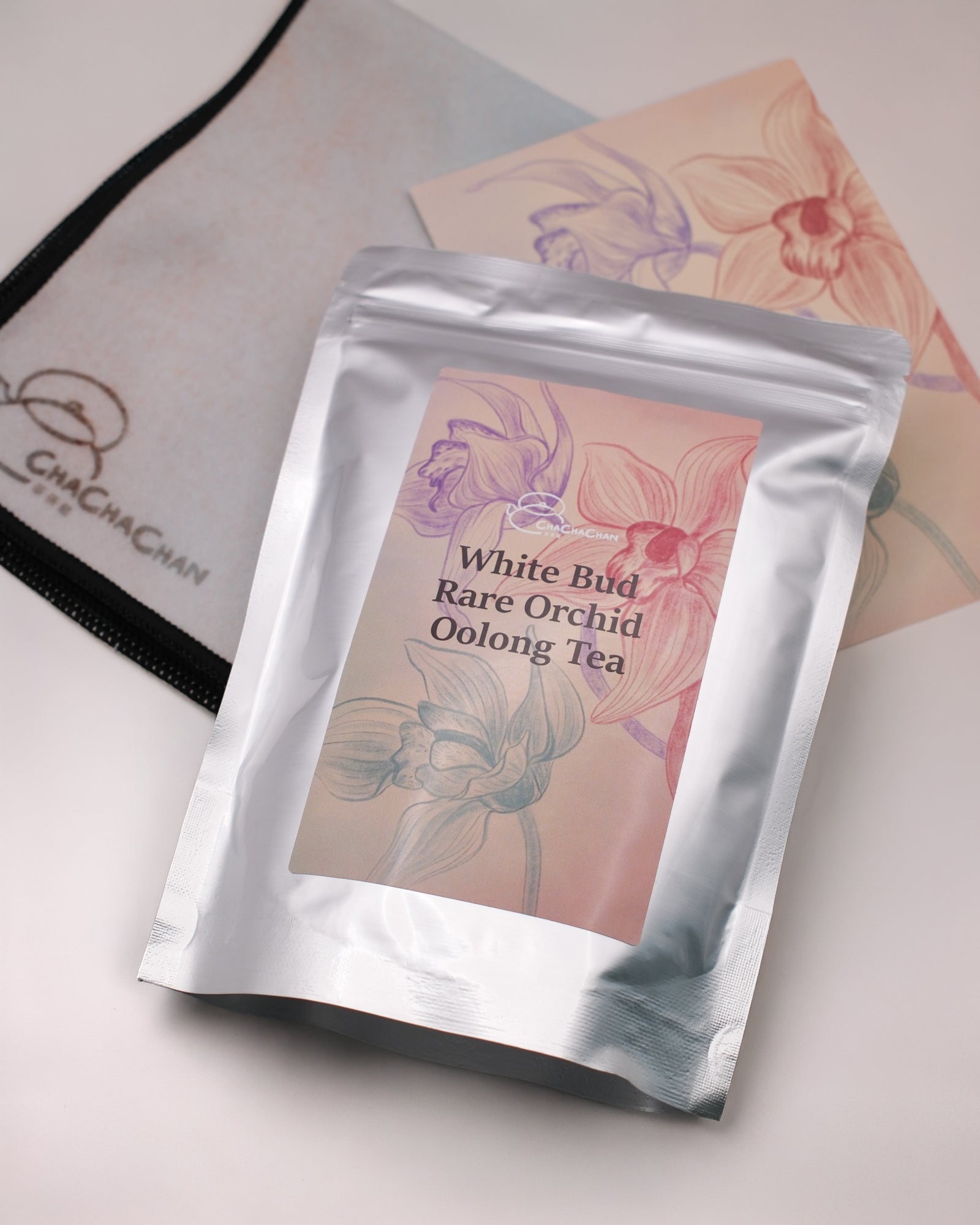 Gift tea set for the 'White Bud Orchid Oolong Tea' from Cha Cha Chan, featuring a packet of loose tea leaves, a postcard, and a reusable magic wrap.